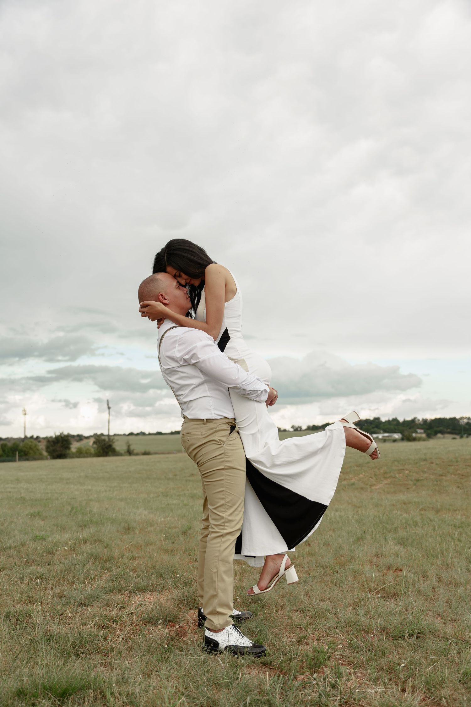 Romantic couple embracing in a grassy field under cloudy skies.