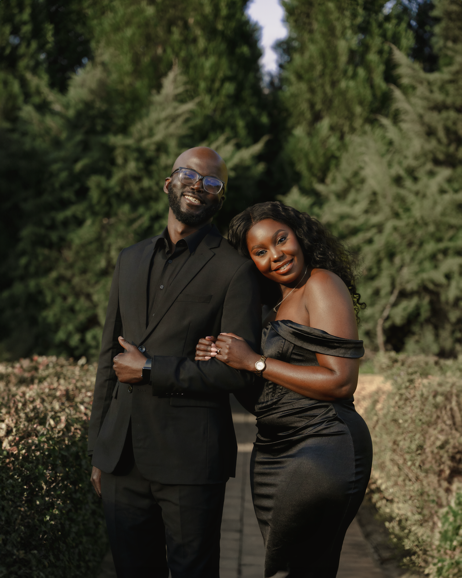 A loving couple poses together outdoors against a backdrop of evergreen trees.