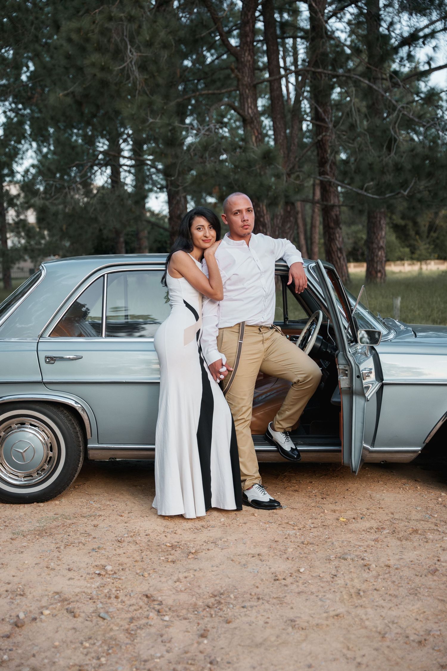 Couple poses against vintage Mercedes-Benz car door in forest setting.