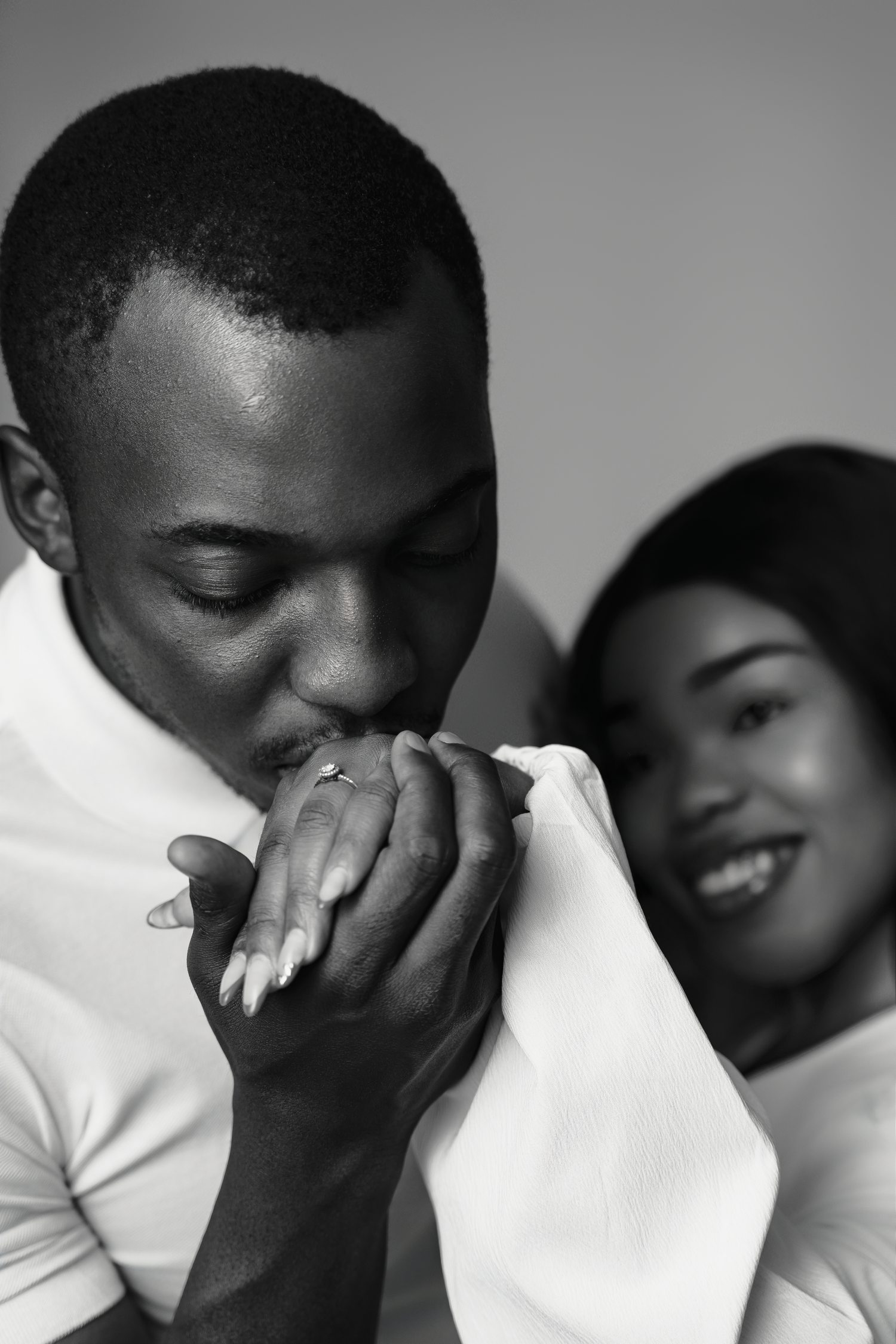 Black and white romantic photo of a couple sharing an intimate moment as one kisses the other's hand tenderly.