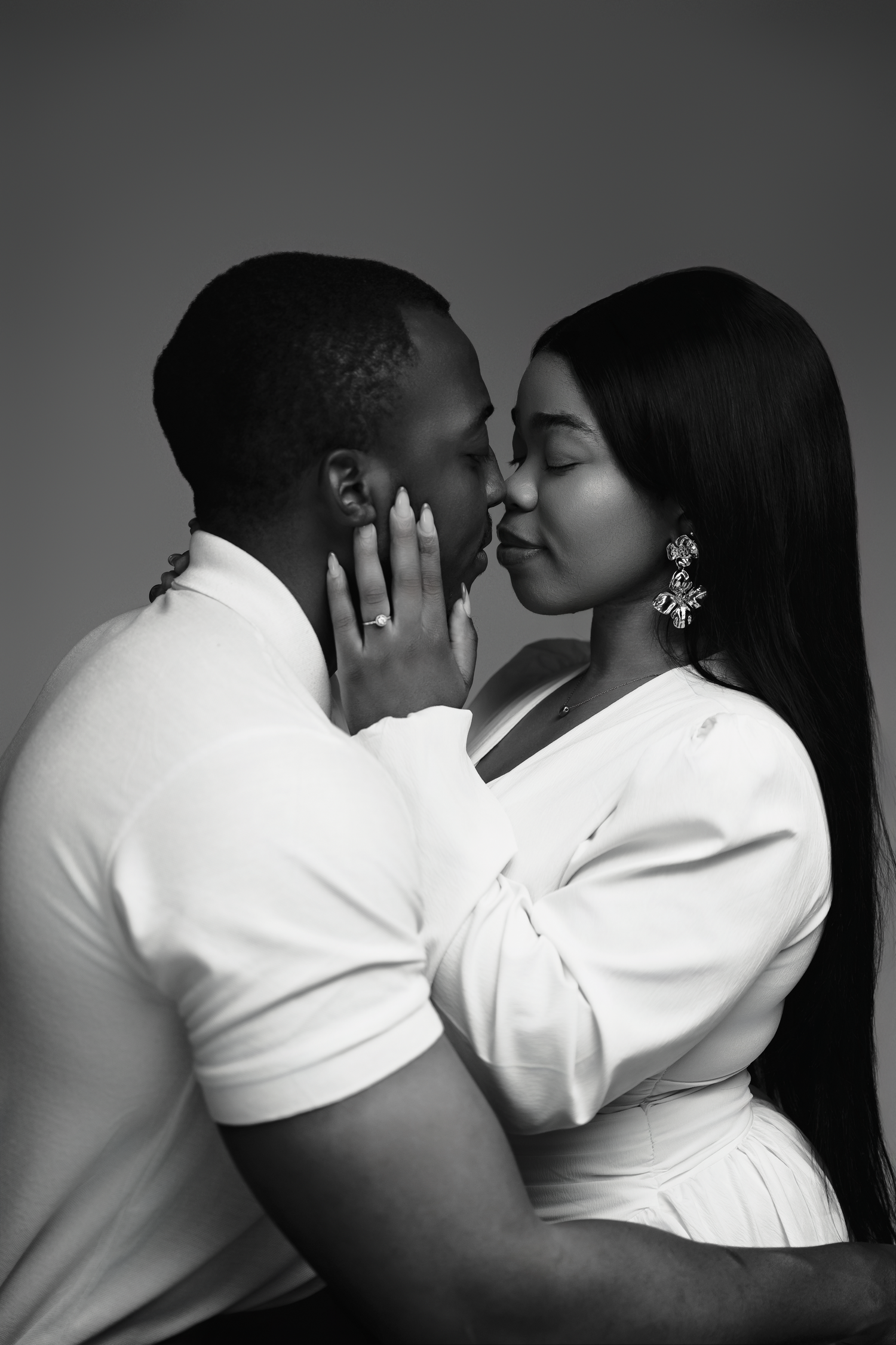 Romantic black and white portrait of a couple in white outfits sharing an intimate moment and tender embrace.