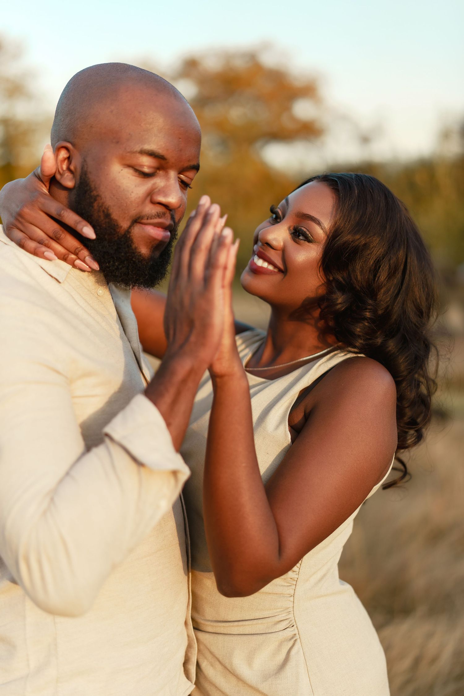 A romantic couple wearing cream colored outfits share an intimate moment outdoors during golden hour.
