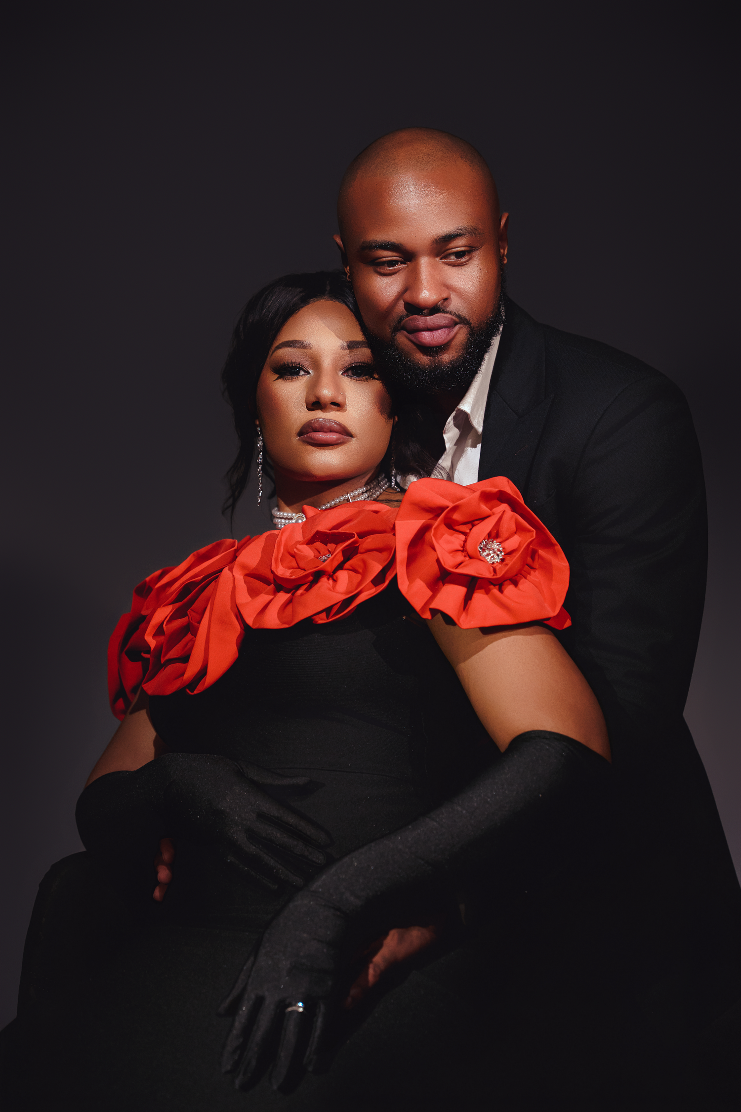 Professional photoshoot featuring dramatic black outfits with vibrant red ruffled accent pieces against dark background.