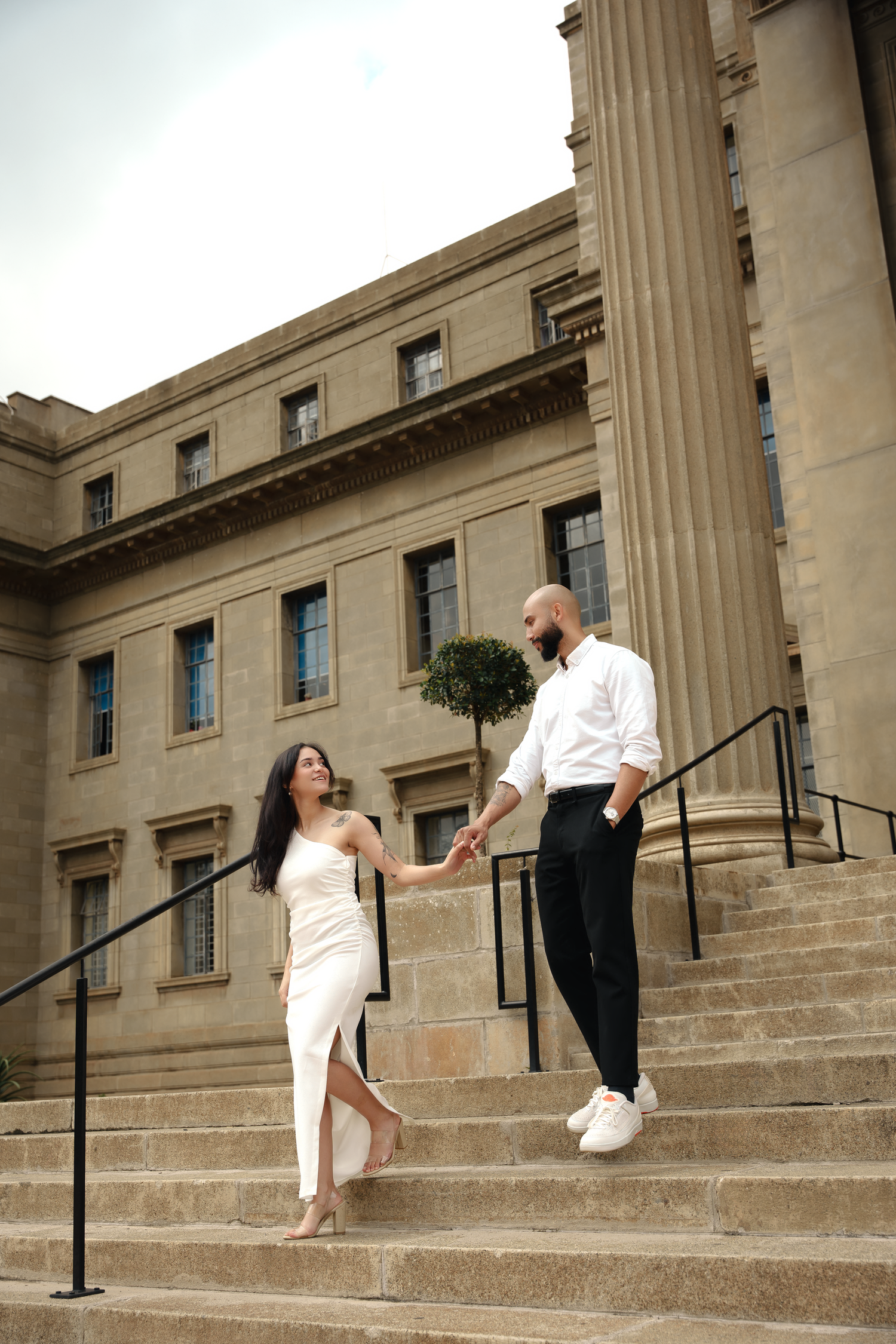 Romantic couple in formal wear interacting on stone steps of neoclassical building.