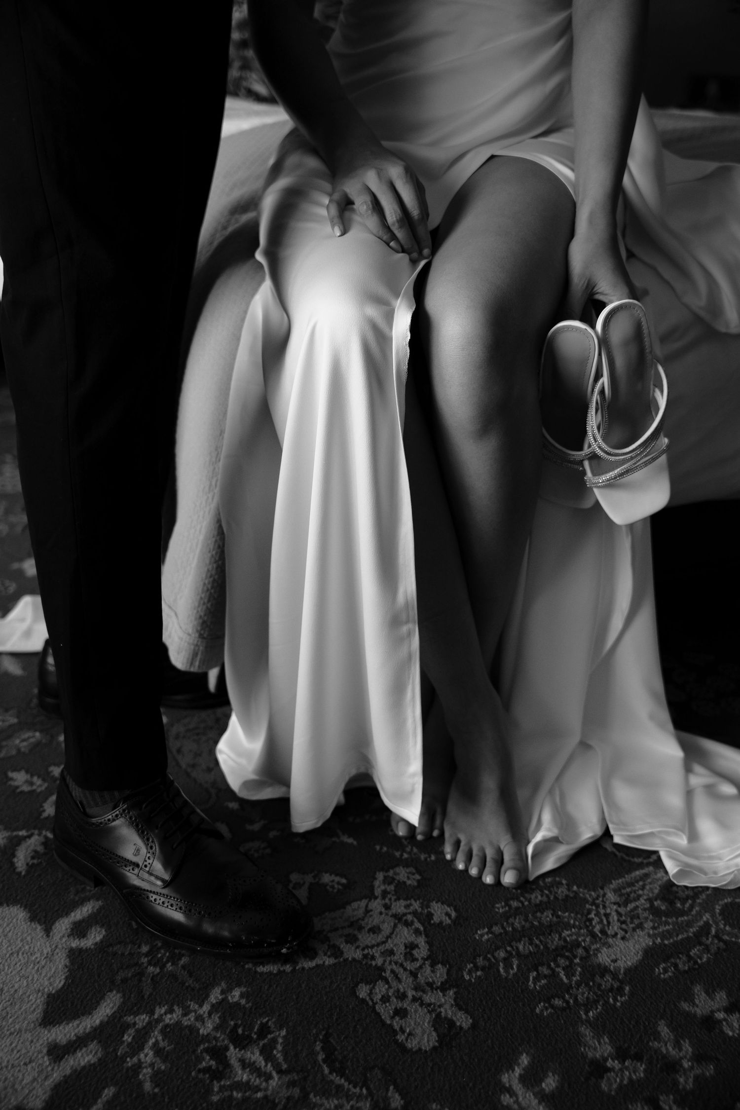Black and white detail shot of bride's dress and groom's shoes during an intimate wedding moment.