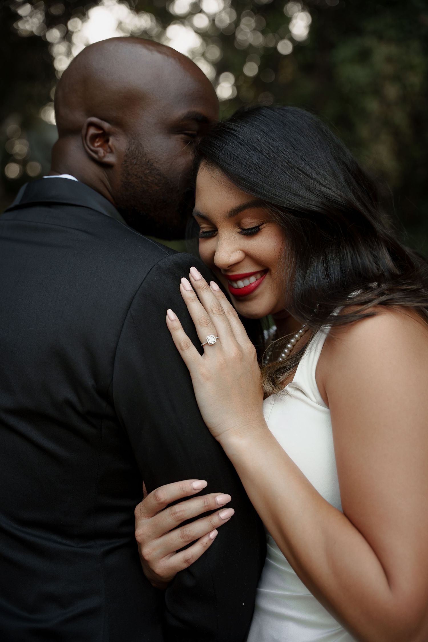A tender moment between newlyweds as the bride shows her ring while embracing her groom outdoors.