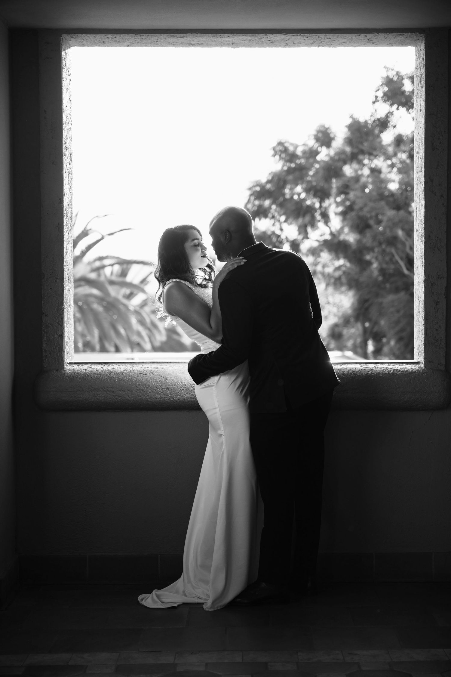 Silhouetted couple shares an intimate moment by a window in black and white photography.