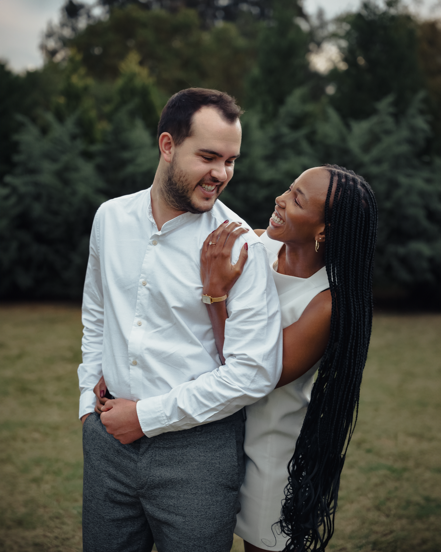 A joyful outdoor couple's portrait captures a tender moment between partners in coordinated white outfits.