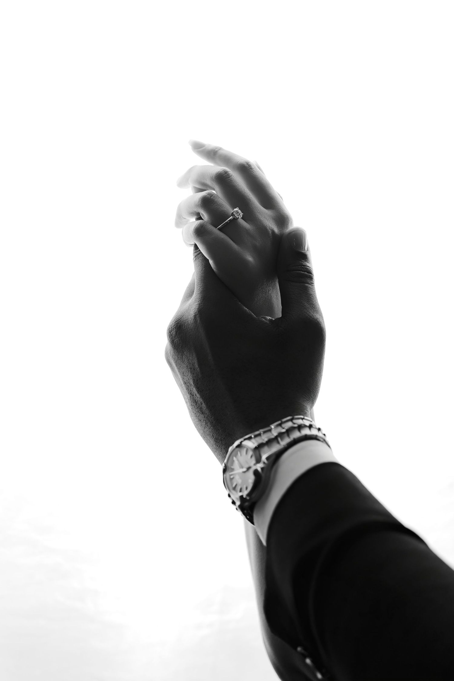 A dramatic black and white close-up of hands clasped together showing jewelry and bracelets.