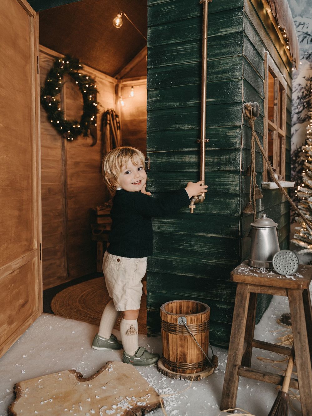 A festive winter scene with wooden barrels and a wreath hanging against a dark green cabin wall.