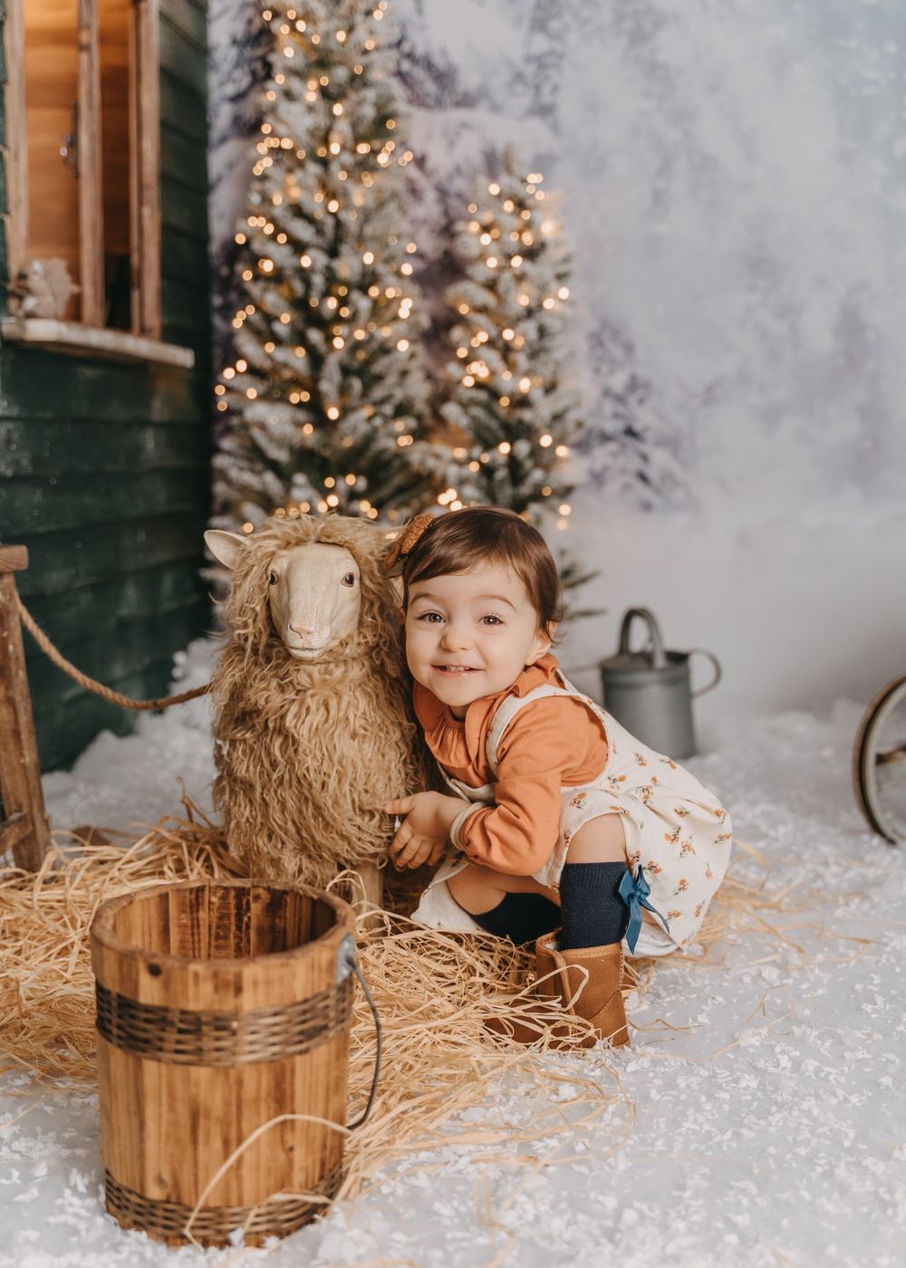 A cozy Christmas scene with a stuffed sheep decoration set against a decorated tree and hay bales in a rustic setting.