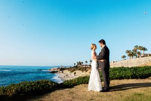 Wedding couple stands along a scenic coastal cliff overlooking the ocean on their special day.