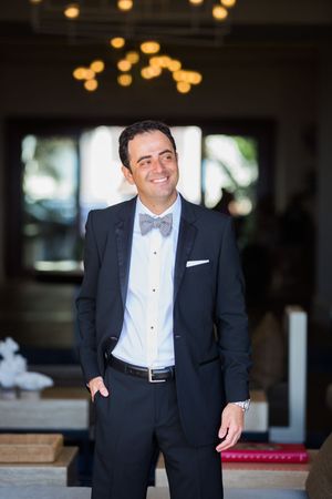 Groom in classic tuxedo and bowtie smiles indoors with warm lighting.