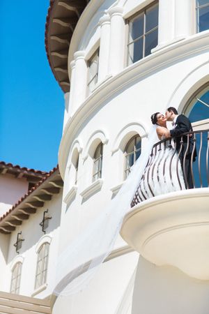 Wedding couple embraces on white Mediterranean-style balcony against blue sky.