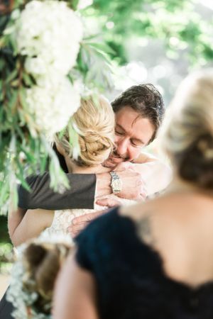 Tender wedding moment surrounded by white floral decorations and greenery.