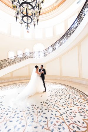 Newlyweds dance in elegant white rotunda with ornate chandelier and patterned floor.
