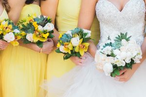 Bridesmaids in yellow dresses hold bouquets of yellow and white flowers next to bride's white gown.