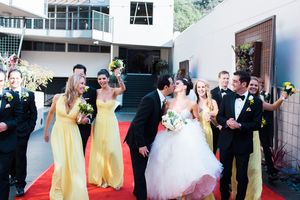 Wedding party poses on red carpet with bridesmaids in yellow dresses and groomsmen in black tuxedos.