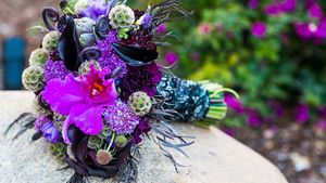 Vibrant purple and blue wedding bouquet with exotic flowers and dark accents.