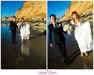 A couple walks along a sandy beach at sunset with dramatic cliffs in the background.