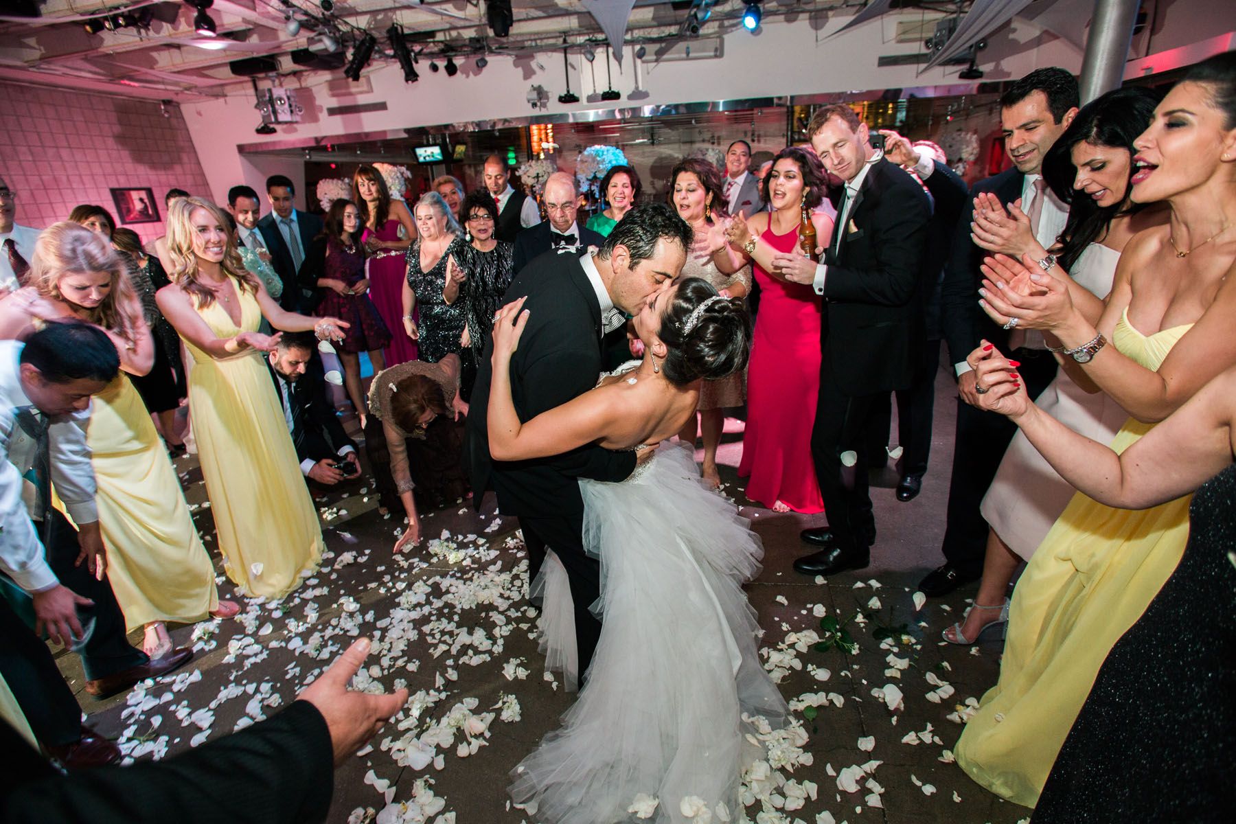 Wedding celebration with confetti falling on dance floor as guests in colorful attire cheer and applaud.