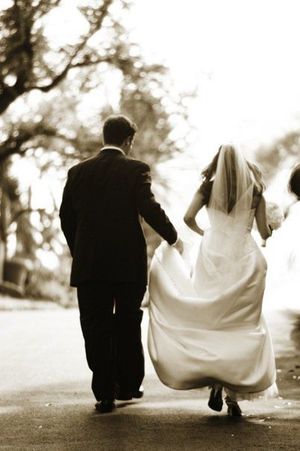 A romantic sepia photo of newlyweds walking together on a path.