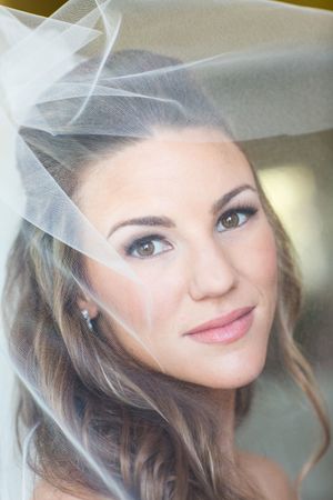 Ethereal bridal portrait through delicate white veil with soft makeup.