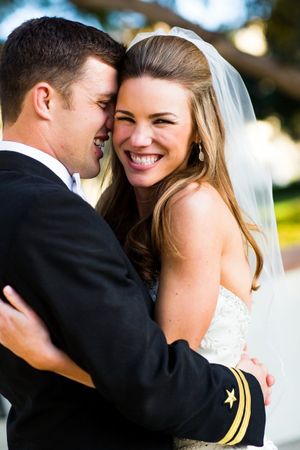 Joyful newlyweds share an intimate moment together outdoors, the bride wearing a white veil and gown.