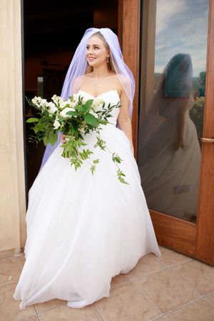 Elegant bride in white ball gown with cascading bouquet of white flowers and greenery.