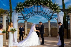 Outdoor wedding ceremony under floral arch with mountain views and clear blue skies.