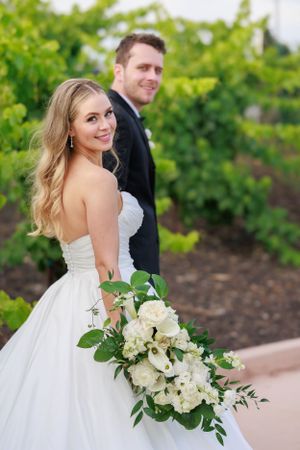 Romantic wedding portrait in vineyard with white floral bouquet.