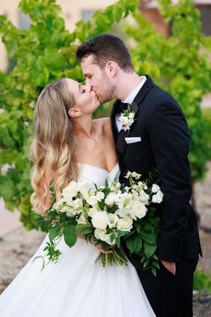 Intimate wedding portrait with white rose bouquet against green vineyard backdrop.
