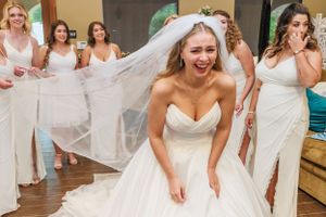 Wedding party celebrating with laughter in white dresses while the bride's veil flows in the breeze.