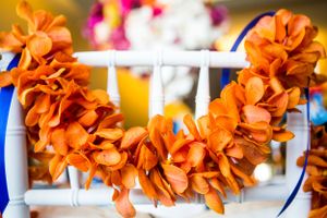 Vibrant orange floral garland decorating a white chair at wedding reception.