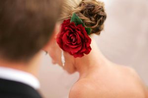 Close-up of an elegant updo hairstyle with a vibrant red rose hair accessory.