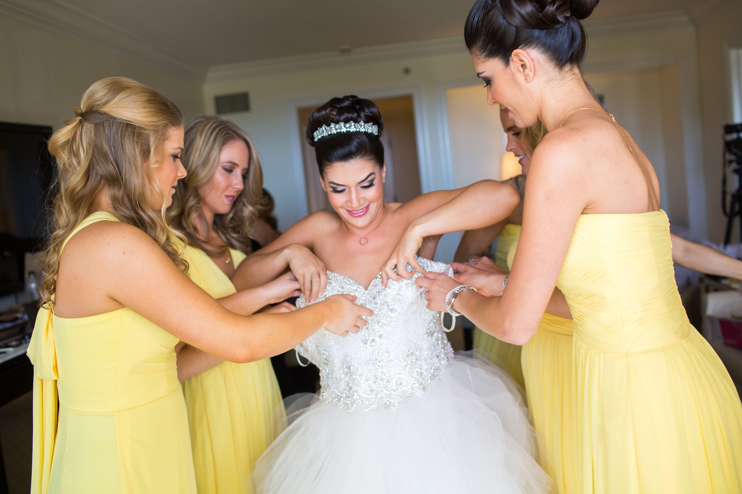 Bridesmaids in yellow dresses help adjust a wedding dress during preparation.
