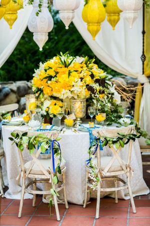 Elegant wedding table setting with yellow floral centerpiece and hanging lanterns.
