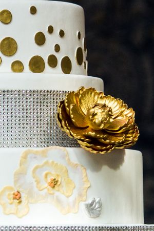 Modern white wedding cake decorated with gold dots, rhinestones and metallic flower details.