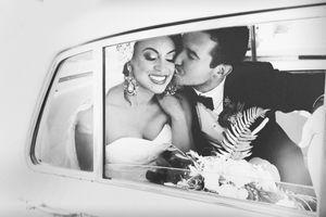 Vintage-style black and white photo of newlyweds sharing an intimate moment in a classic car.