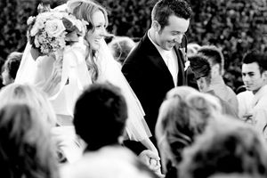 A black and white wedding ceremony photo showing a couple surrounded by guests.