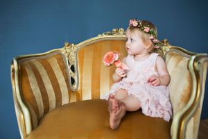 Little girl in pink dress with flower crown sitting on vintage gold settee.