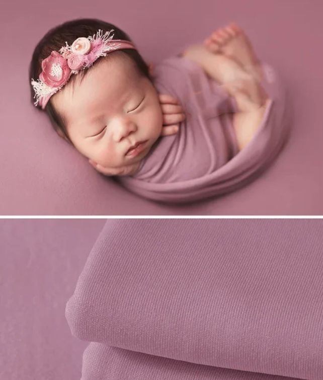 Newborn baby wrapped in soft purple fabric with delicate pink floral headband sleeping peacefully.