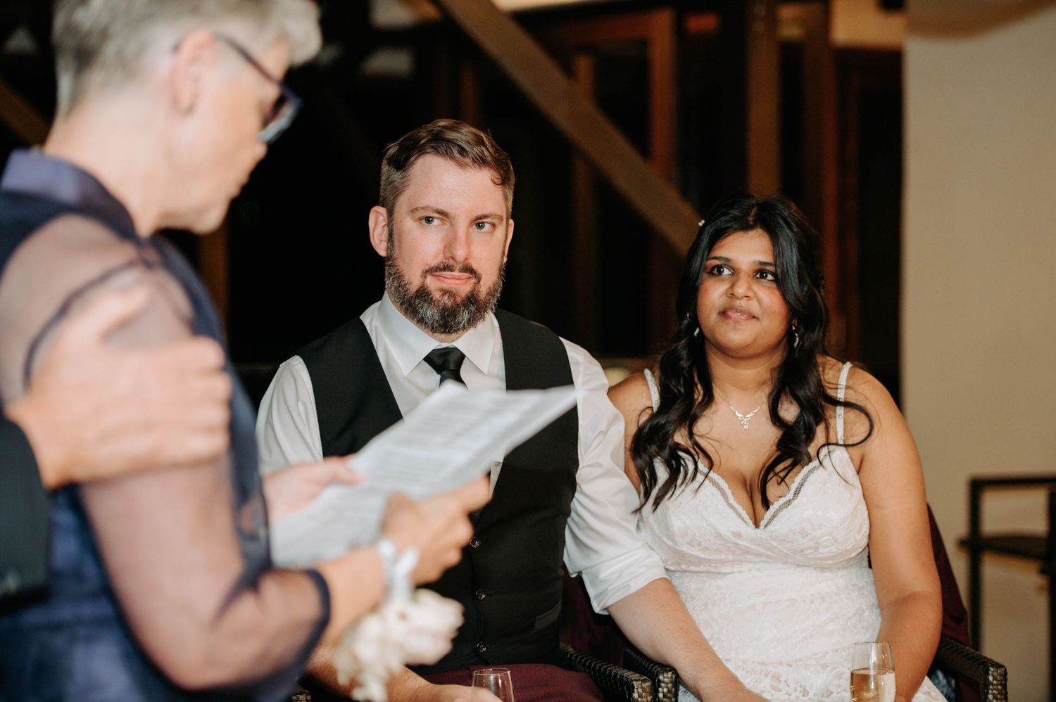 A couple listens to a speech during their indoor wedding reception.