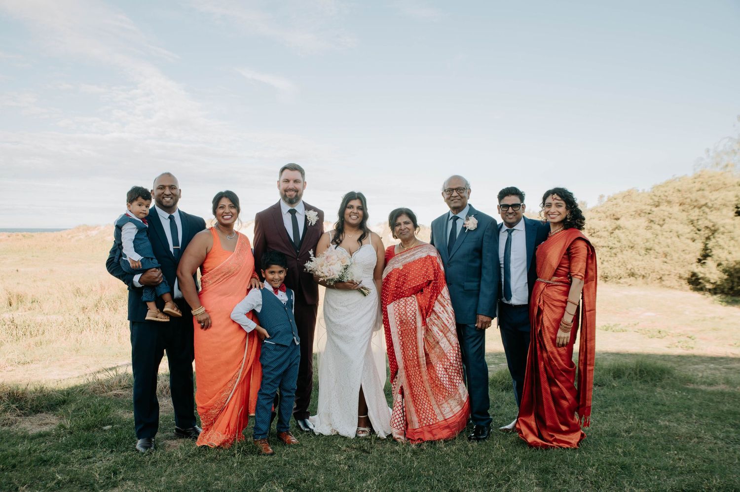A wedding party poses together outdoors wearing vibrant orange and blue attire.