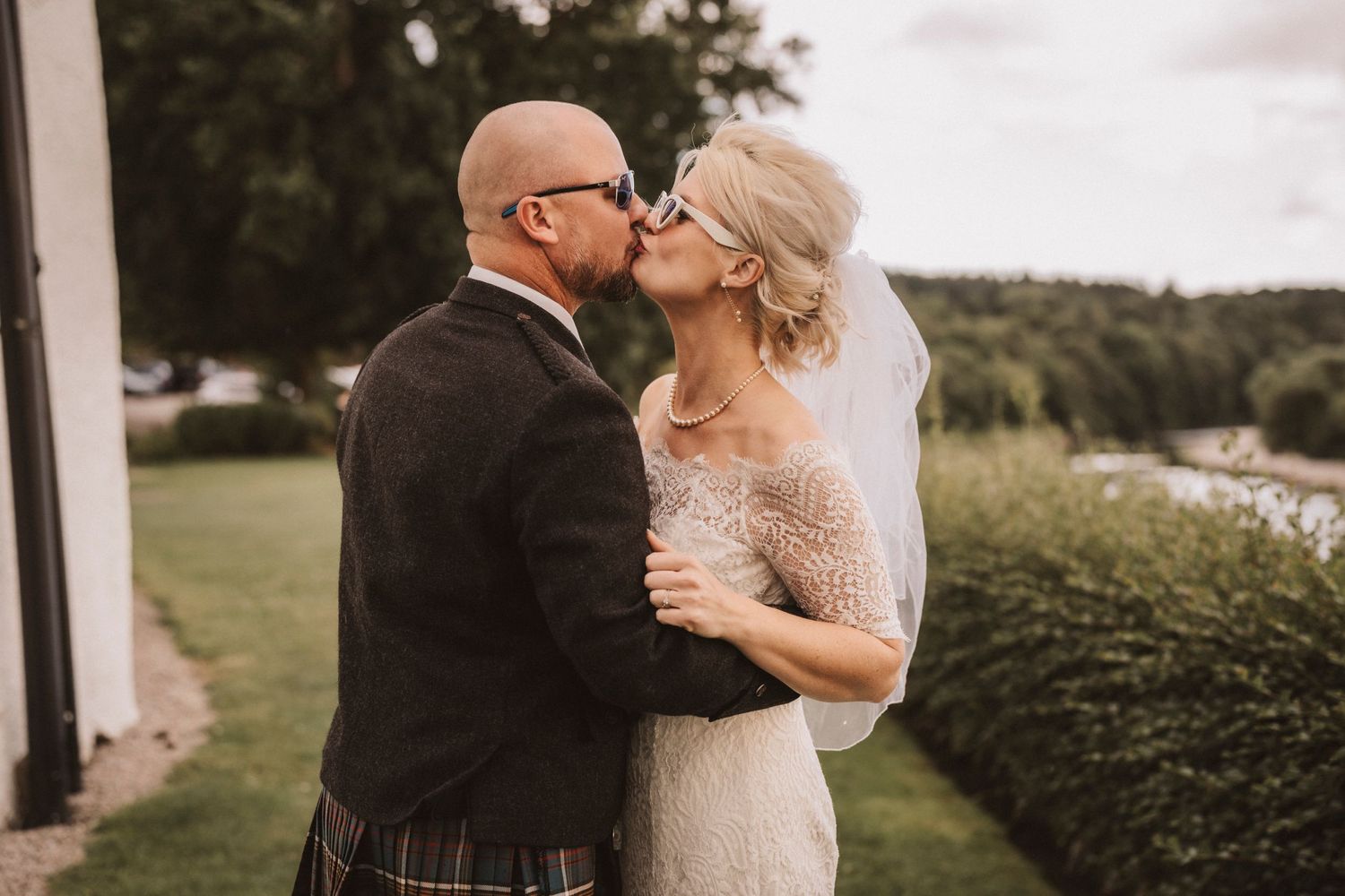 Romantic outdoor wedding kiss with groom in Scottish attire and bride in lace dress.