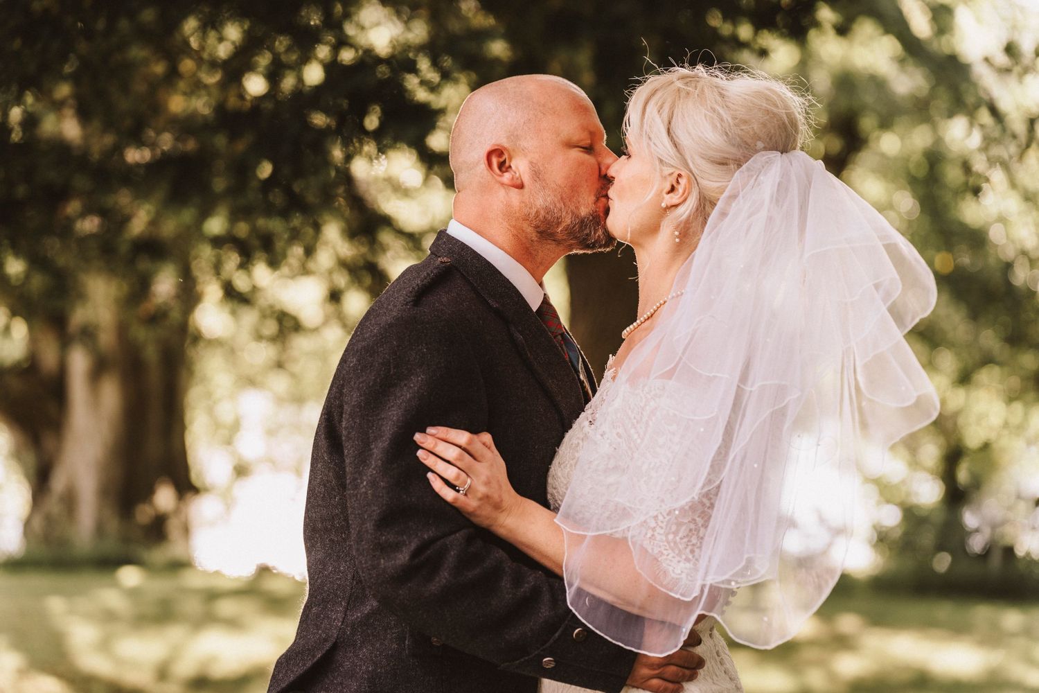 Romantic wedding portrait of newlyweds embracing outdoors in Scottish wedding attire.