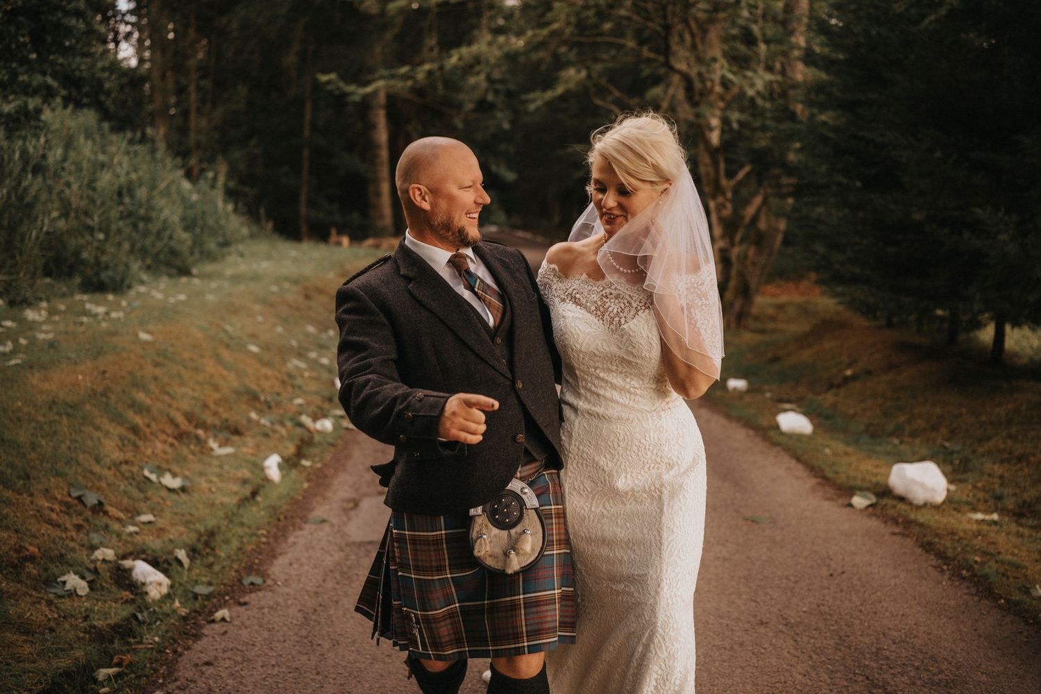 Wedding couple walking along a forest path with groom wearing traditional Scottish kilt.