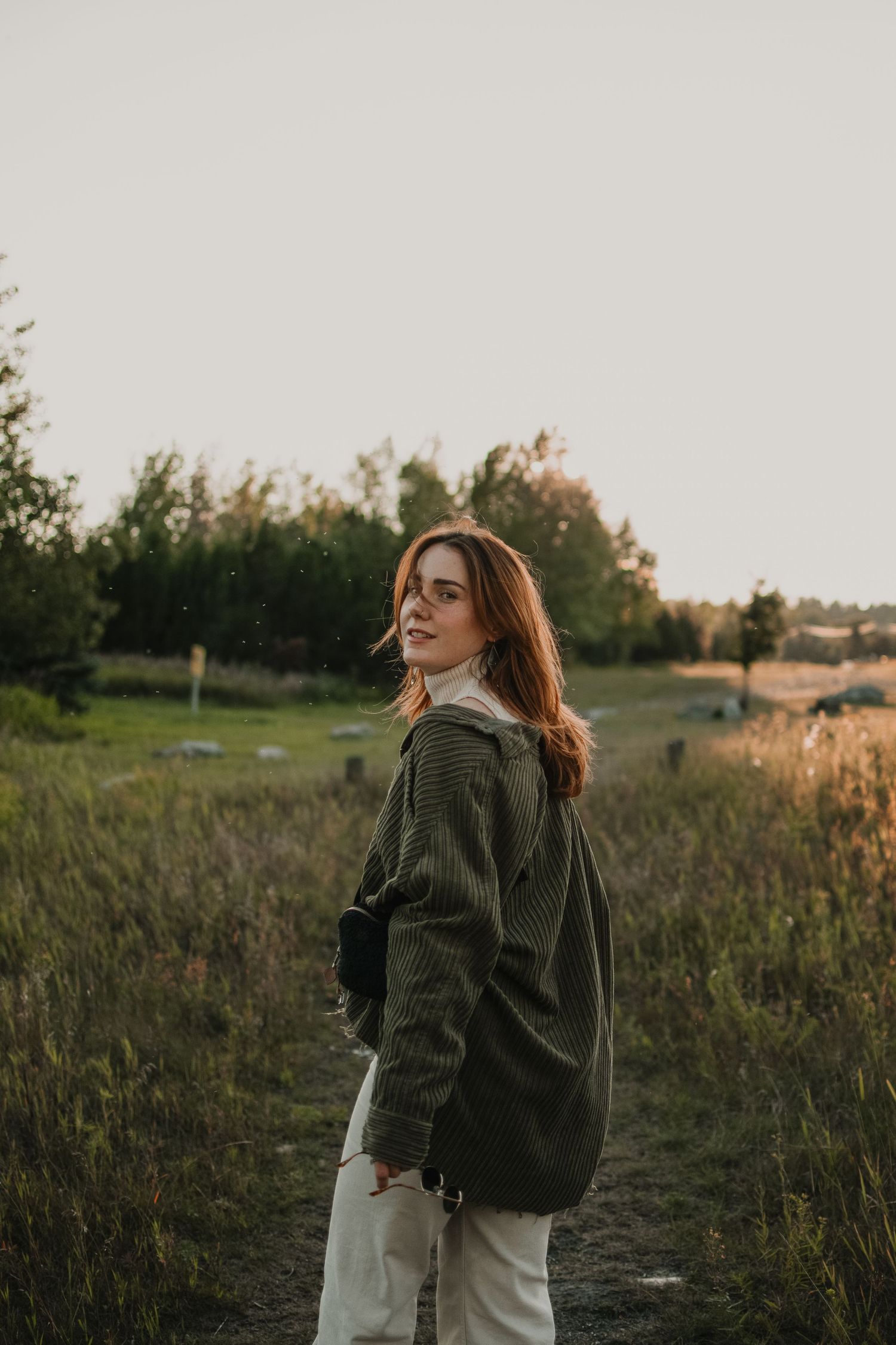 A figure in an oversized jacket stands in a sunlit field at golden hour.