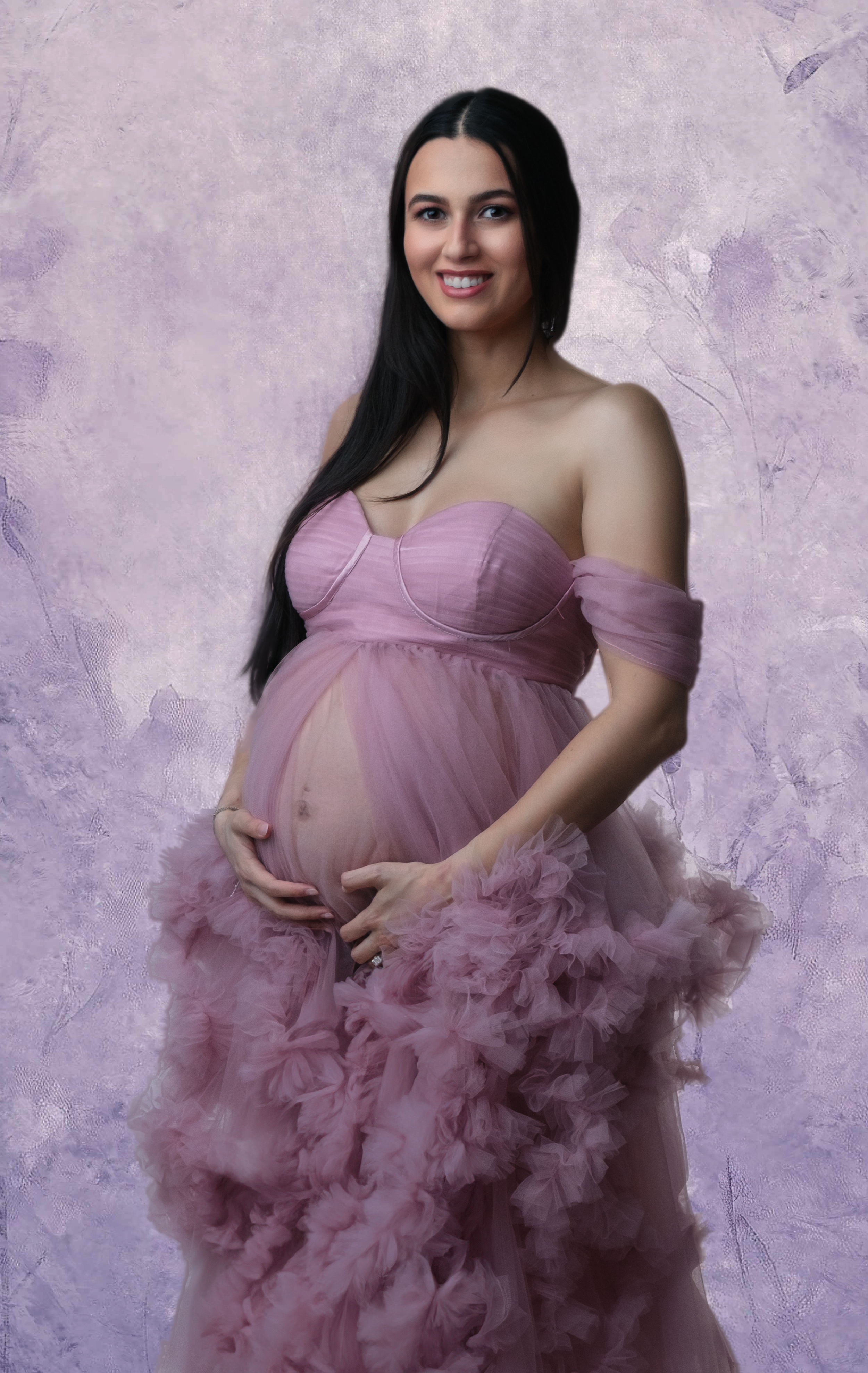 Maternity portrait in flowing pink tulle gown against purple backdrop.