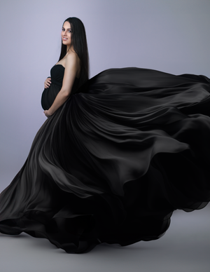 Dramatic maternity photo with flowing black dress against purple background.